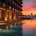 Rooftop infinity pool at a luxury hotel glowing at sunset, with chic loungers and a glittering city skyline reflected in the still water.